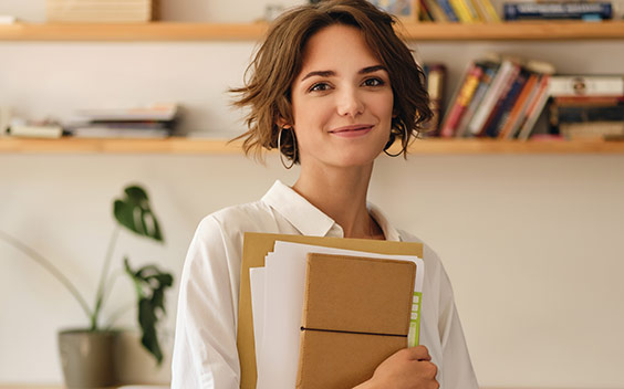 Young white woman holding notebooks and smiling.